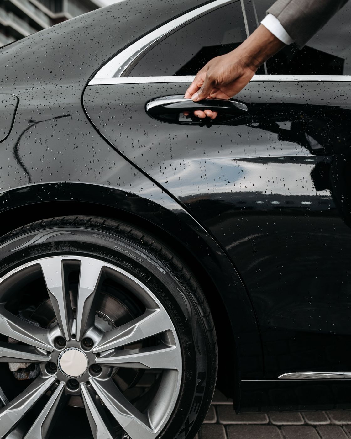 A chauffeur in a dark suit holding open the rear door of a black car