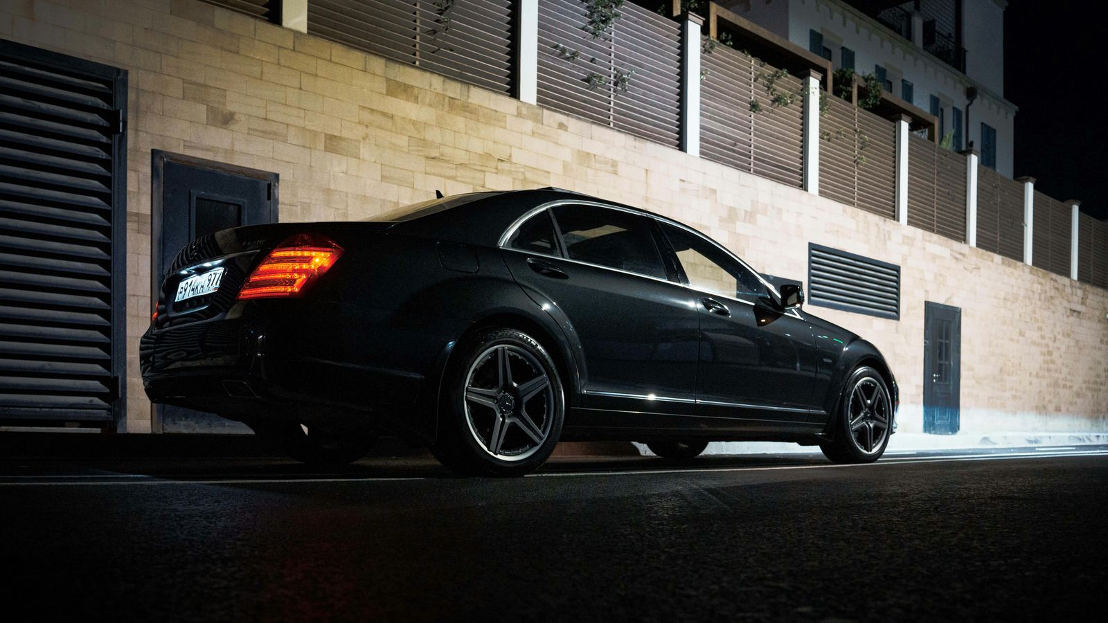A black sedan waiting at a lit entrance at night